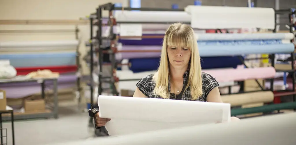 dmo administration team member looking at a pattern in the factory with roles of fabric behind