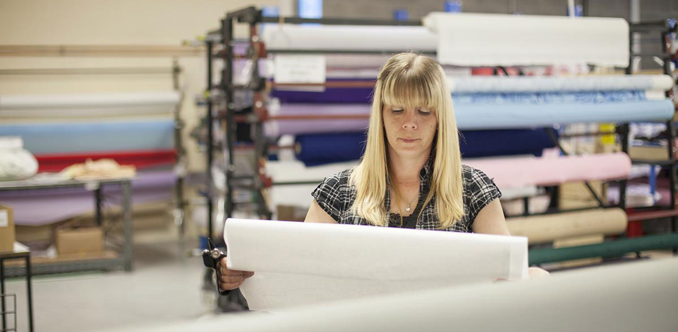 dmo administration team member looking at a pattern in the factory with roles of fabric behind