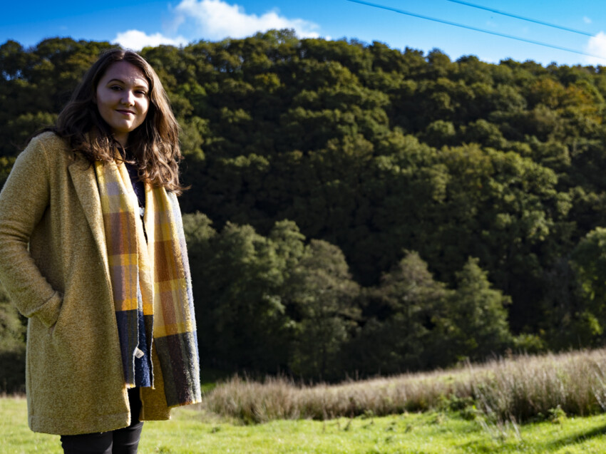 Chloe Sharland, DMO patient, standing in a yellow coat in a field in front of trees