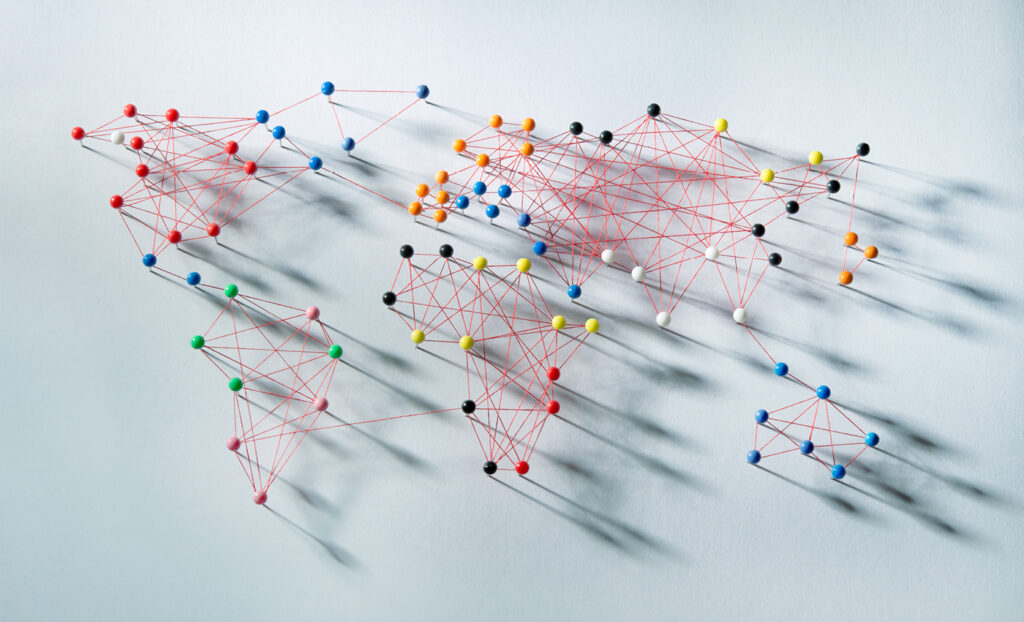 Pins in a white board with string around them showing a world map