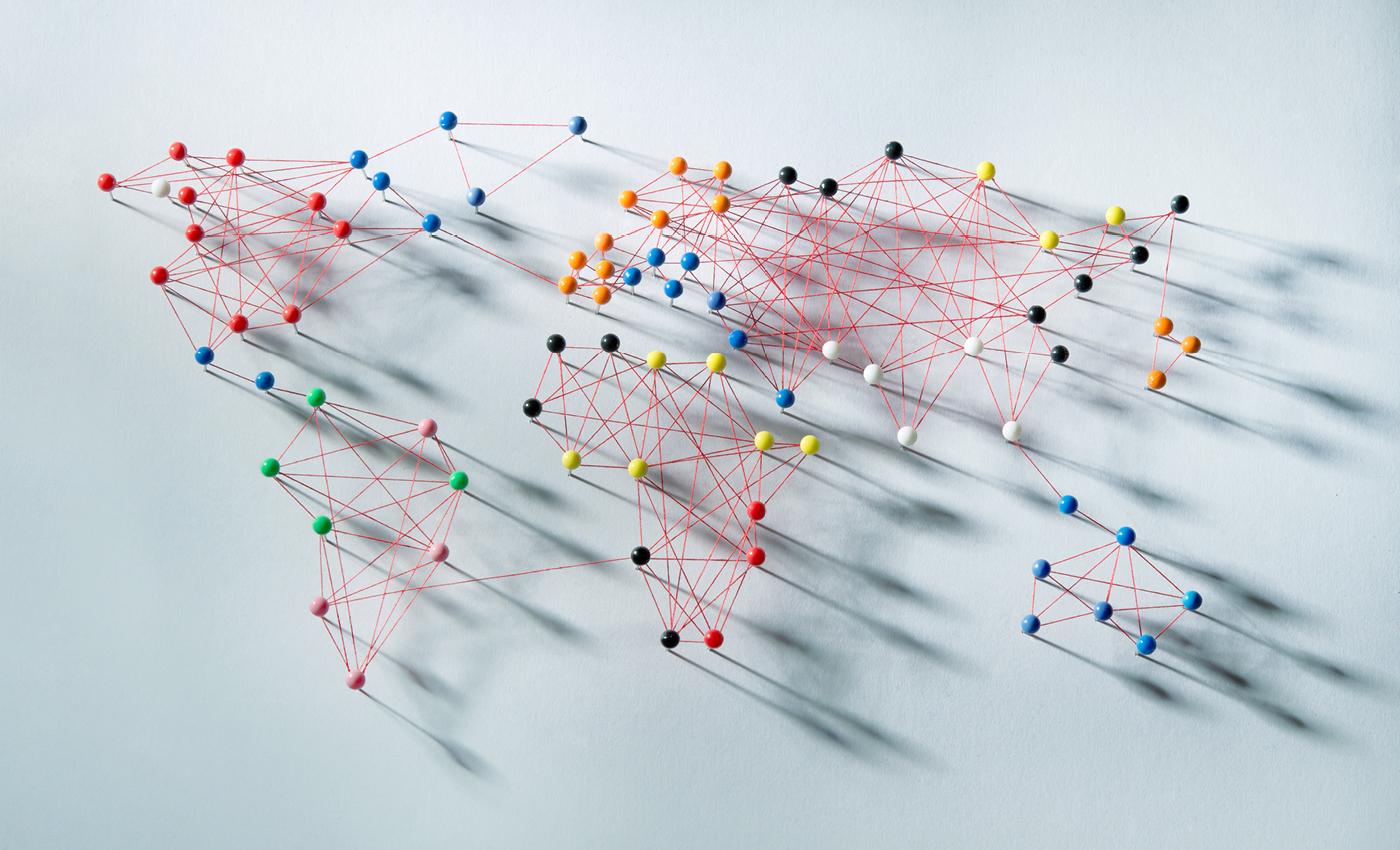 Pins in a white board with string around them showing a world map