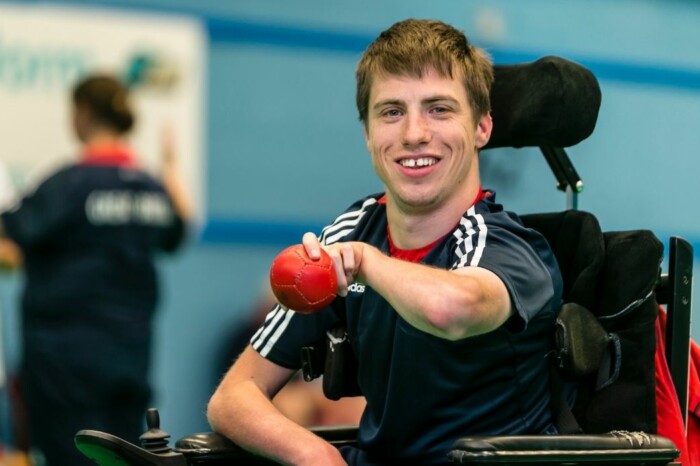david smith holding a boccia ball sat in his chair smiling