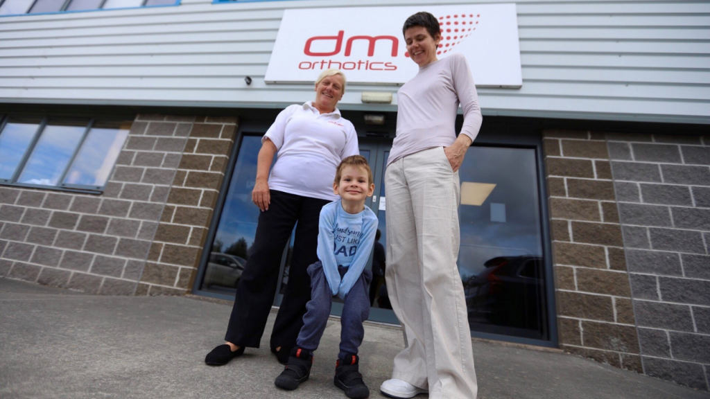 jakov standing crouched outside the DMO factory with Pam and his mother