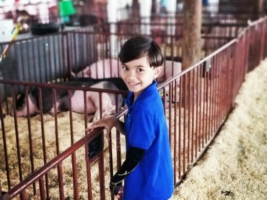 jai stood at a petting zoo smiling at the camera wearing a blue t shirt and his dmo glove